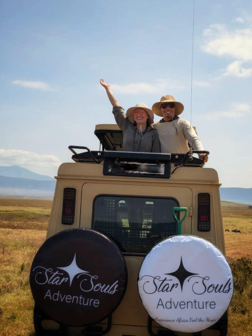 Two delighted Star Souls guests cheering from the roof hatch of their safari vehicle in the Ngorongoro Crater