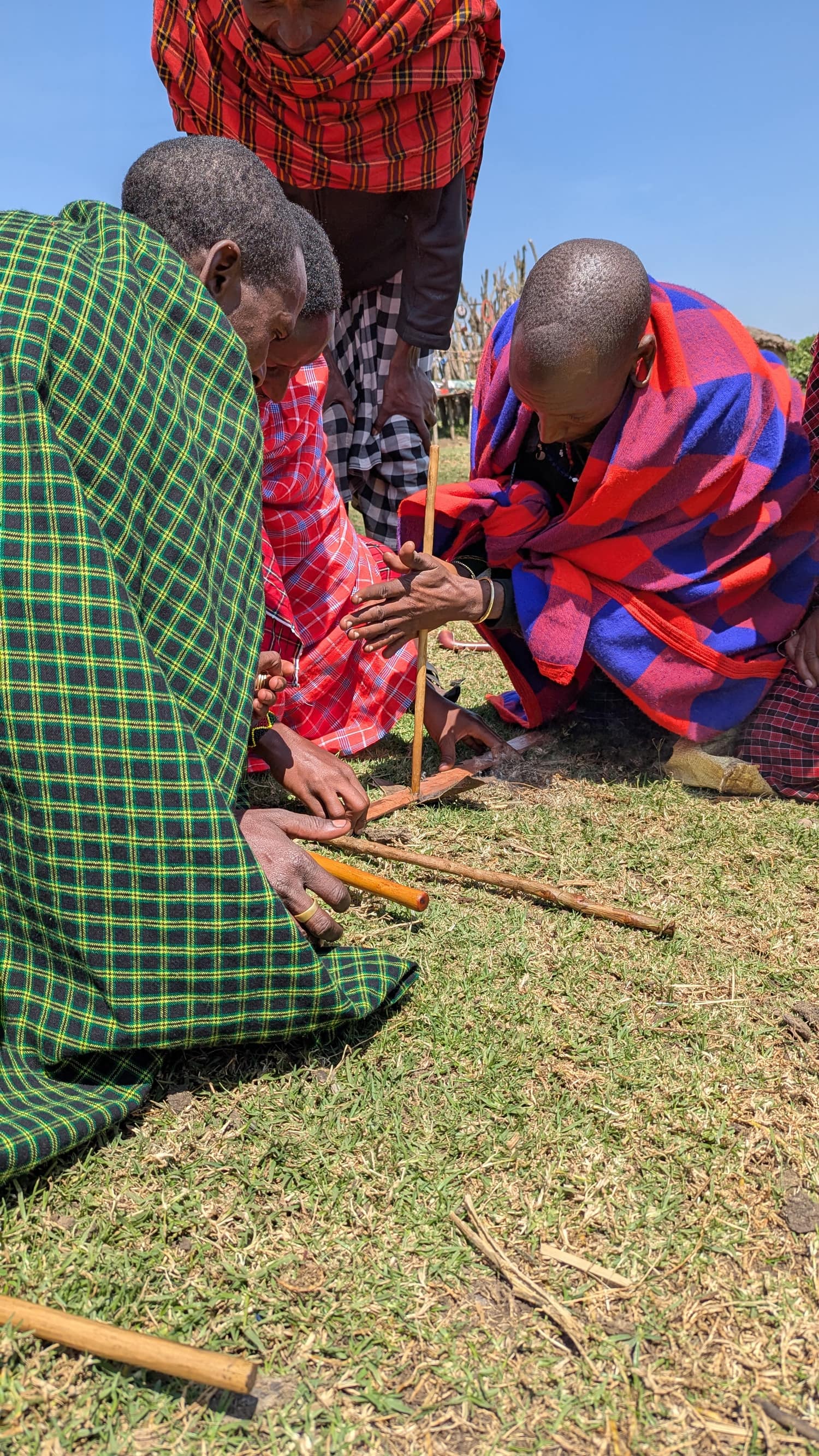 Maasai elders in traditional robes making fire by hand with friction sticks